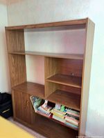 Front view of tall brown engineered wood bookcase showing open shelves, cabinet door and cubby layout