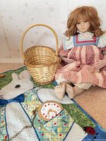 Doll seated beside wicker basket on quilted rabbit runner showing included watch charm