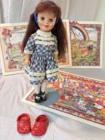 Front view of doll on stand with dress, black shoes, red crocs in foreground