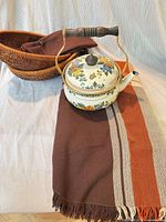 All items grouped: enamel floral teapot, wicker basket, brown striped tablecloth, brown napkins