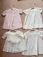 Four dresses laid out: pink top left, white top right, off-white bottom left, white scalloped hem bottom right