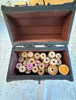 Open wooden box showing red fabric lining and multiple wooden thread spools inside