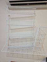 Front view of white wall-mounted wire shelf showing four tiers and side basket