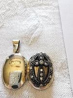 Front and interior of oval sterling silver locket showing cross design and crystal detailing