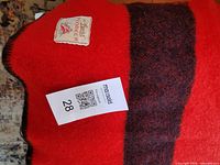 Overall view of bright red wool blanket with black stripe and tag visible