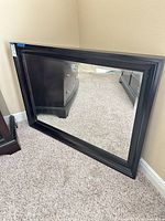 Angled view of entire mirror leaning against wall showing dark brown wood frame and reflection