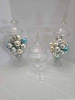 Front view of all three clear glass pedestal apothecary jars with ornaments