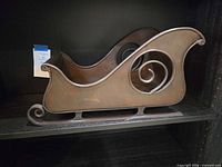 Full view of bronze metal sleigh on shelf, showing front and side scroll detail