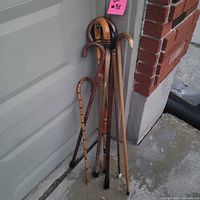 Seven assorted wooden crook canes leaning against garage