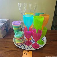 Grouped coloured and clear plastic wine glasses, stacked Manna cups, round tray