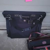 Front view of black garment bag with hardware and logo medallion