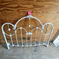 Front view of white enamel iron headboard with brass and porcelain details