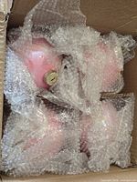 Four pink glass ornaments wrapped in bubble wrap inside box