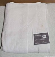Folded white Hydra Spa towel with front brand tag visible
