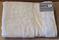 Folded beige bath towel showing terry texture and weave band