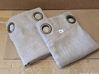 Pair of folded taupe curtain panels with grommets visible