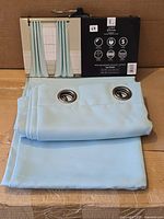 Folded blue curtain panels showing metal grommets and packaging header