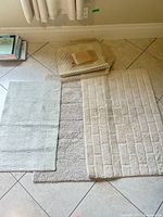 Three bath rugs laid out with stack of mesh pads and underpadding pieces