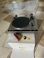 Turntable on original box with dust cover open, adapters and red case visible