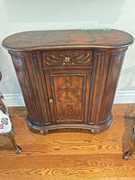 Front view of closed cabinet showing serpentine shape, drawer, door, fluted columns, bun feet