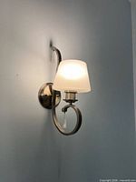 Mounted view of one brushed nickel wall sconce with frosted glass shade and crystal drop pendant