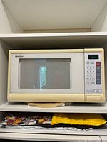 Front view of Quasar beige countertop microwave on shelf