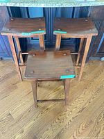 Three wooden stools showing two tall and one shorter with square saddle seats