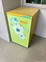 Front angled view of yellow cabinet with green floral door
