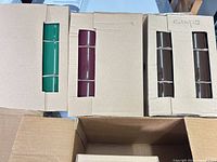 Boxes containing green, burgundy and brown mugs, three per carton visible