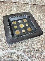 Entire tray top view showing square form, black paint, zig-zag inner rim and nine embedded coins