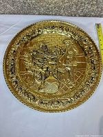 Front view of brass plaque showing embossed musicians scene and floral border