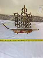 Front view of wooden sailboat showing painted hull lettering and yellow cord rigging with measuring tape for scale