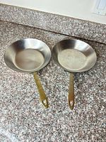 Top view of both pans showing stainless interiors and brass handles