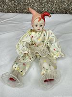 Front view of porcelain head clown doll sitting, costume and hat visible