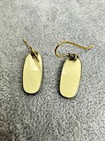 Front view of both cream enamel earrings on grey background