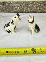 Both dog figurines side by side with tape measure for scale