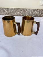 Front view of both brass mugs displaying overall design and patina