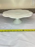 Side view of white porcelain pedestal cake stand with measuring tape showing diameter