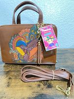 Front view showing hummingbird artwork, handles, tag, detachable strap
