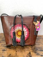 Front view of brown leather tote with floral appliqué and tassels