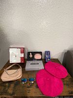 Group shot showing all items: sunglasses, watch in box, coin purse, shoulder bag, two pink berets, boxed greeting cards, boxed earrings set