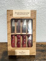Front of boxed Porterhouse steak knife set showing four knives with red riveted handles