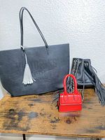 All three bags displayed: Victoria's Secret tote, black bucket bag, red mini bag