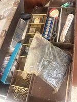 Open brown tackle box showing compartments with bobber, swivels, line spool and bag of tackle