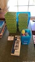 Overall lot showing green baskets, blue bins, blue tote, decorative eggs, and tea-light pack
