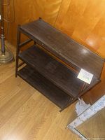 Front angled view of shelving unit showing three dark brown laminate shelves and metal frame
