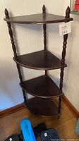 Full view of the assembled four-tier dark brown wooden corner shelf showing shape, shelves, legs and finials