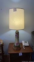 Full view of assembled lamp on table showing ceramic base, metal footing and fabric shade