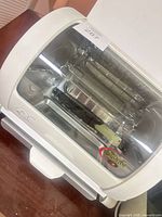 Front view of George Jr. white countertop rotisserie oven showing glass door and interior spit rod