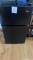 Front view of black Midea compact refrigerator showing two doors and overall condition